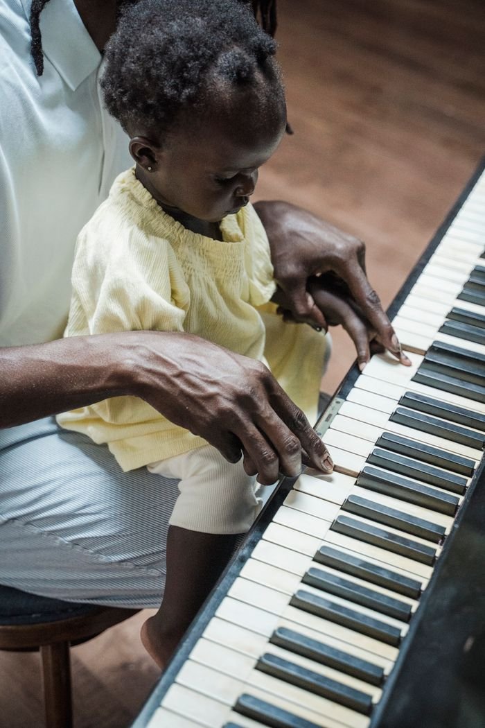 A child learning to play the piano with an adult's help, emphasizing family bonding and education