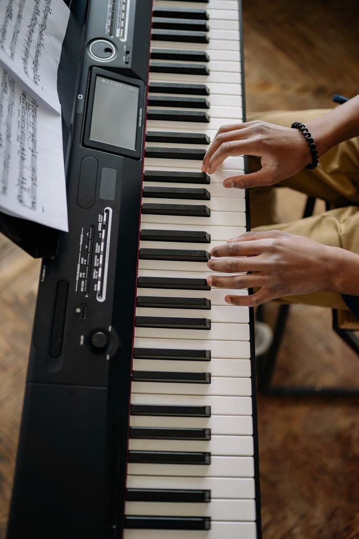 High angle view of hands playing an electronic keyboard with sheet music on top.